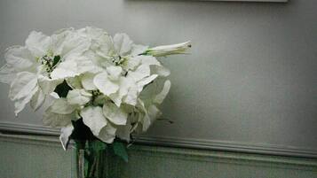 A white vase with white flowers on a dark wooden table, a framed picture on the wall, and a bowl of pebbles on the table.