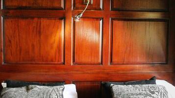 A hotel room with a wooden paneled wall, a bed with patterned pillows, and a wall-mounted lamp.