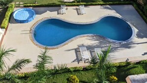 Une piscine avec deux chaises longues et des parasols, entourée d’une pelouse bien entretenue et de palmiers.