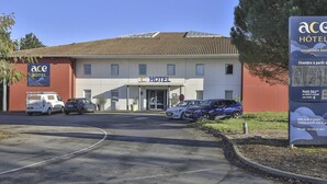 Een hotel met een bord waarop 'ACE HOTEL' staat, en een parkeerplaats met verschillende auto's.