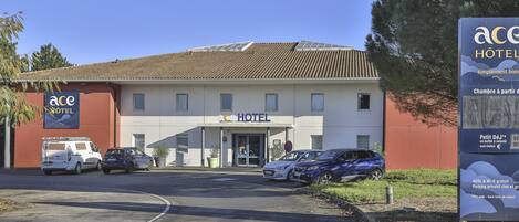 A hotel with a sign reading "ACE HOTEL" and a parking area with several cars.
