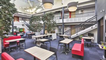 A spacious indoor area with multiple tables and chairs, a staircase, and potted plants.