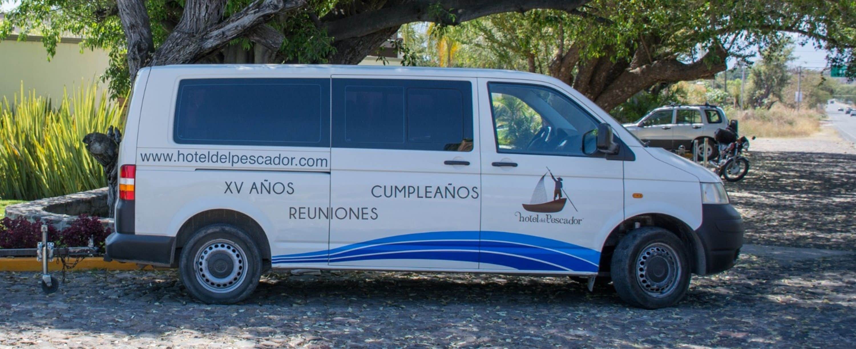 A white van with "Hotel del Pescador" and "XV Anos Reuniones" on its side, parked on a cobblestone street.