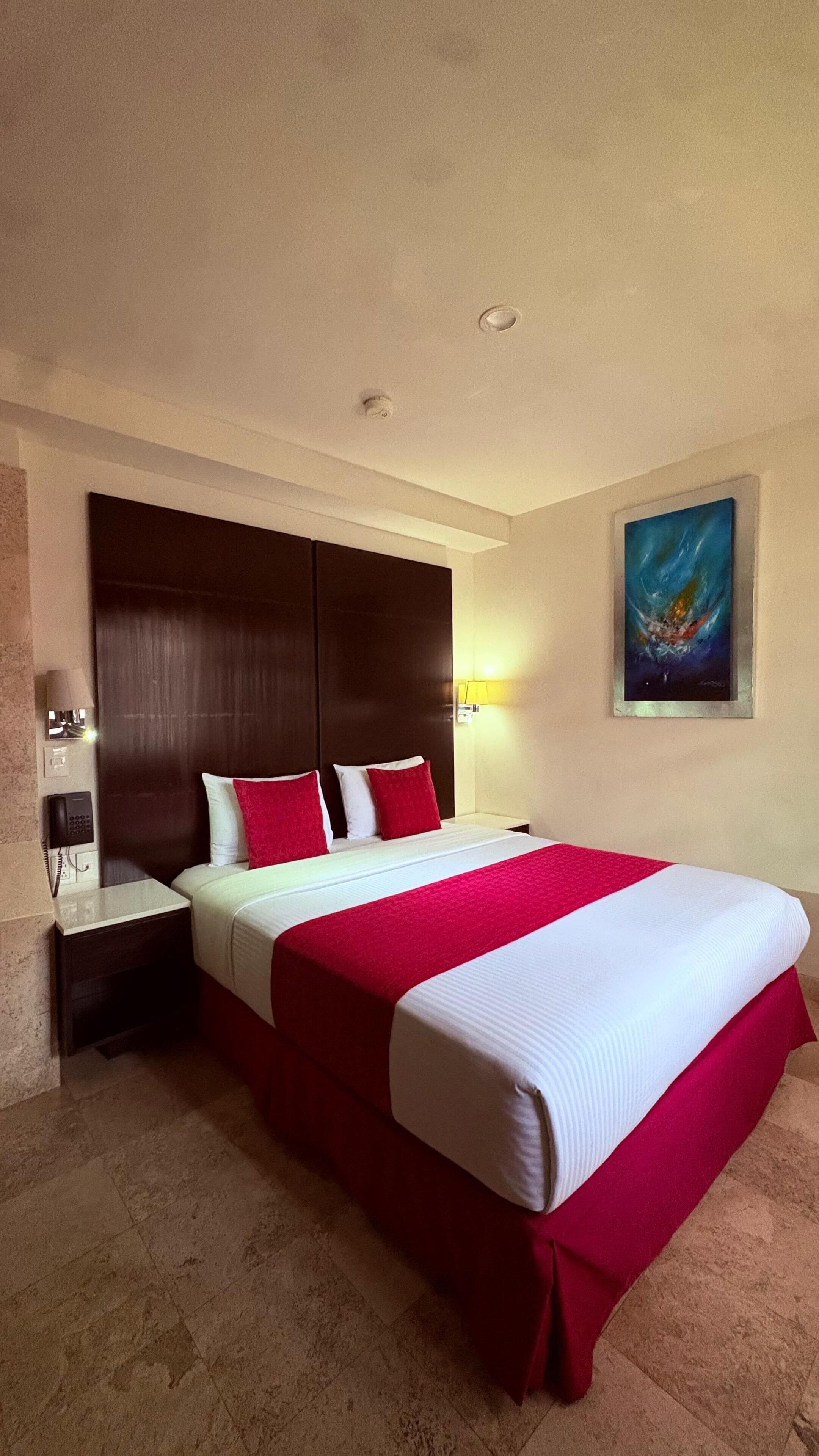 Una habitación de hotel con una cama grande, una mesita de noche, un teléfono y un cuadro en la pared.