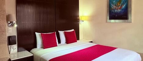 A hotel room with a large bed, a nightstand, a phone, and a painting on the wall.