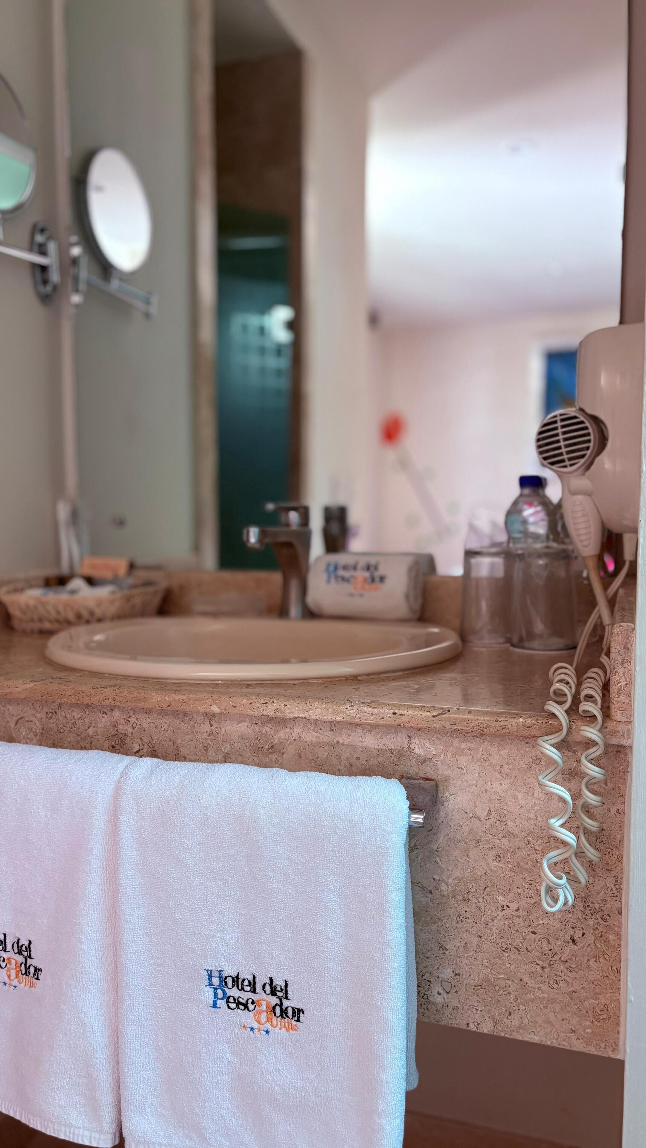 Une salle de bain équipée d’un lavabo, d’un miroir, d’une serviette et d’un sèche-cheveux.