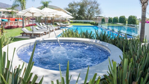 A hot tub surrounded by lounge chairs and umbrellas, with a pool and greenery in the background. - Hotel del Pescador (Jocotepec)