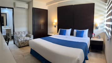 Habitación de hotel con una cama grande, una silla, un armario, un escritorio con lámpara y un equipo de aire acondicionado.
