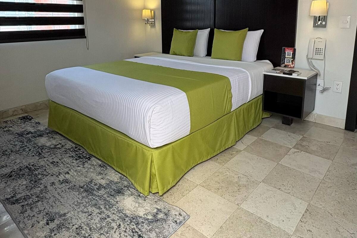 A hotel room with a large bed, a nightstand with a phone, and a window with blinds.