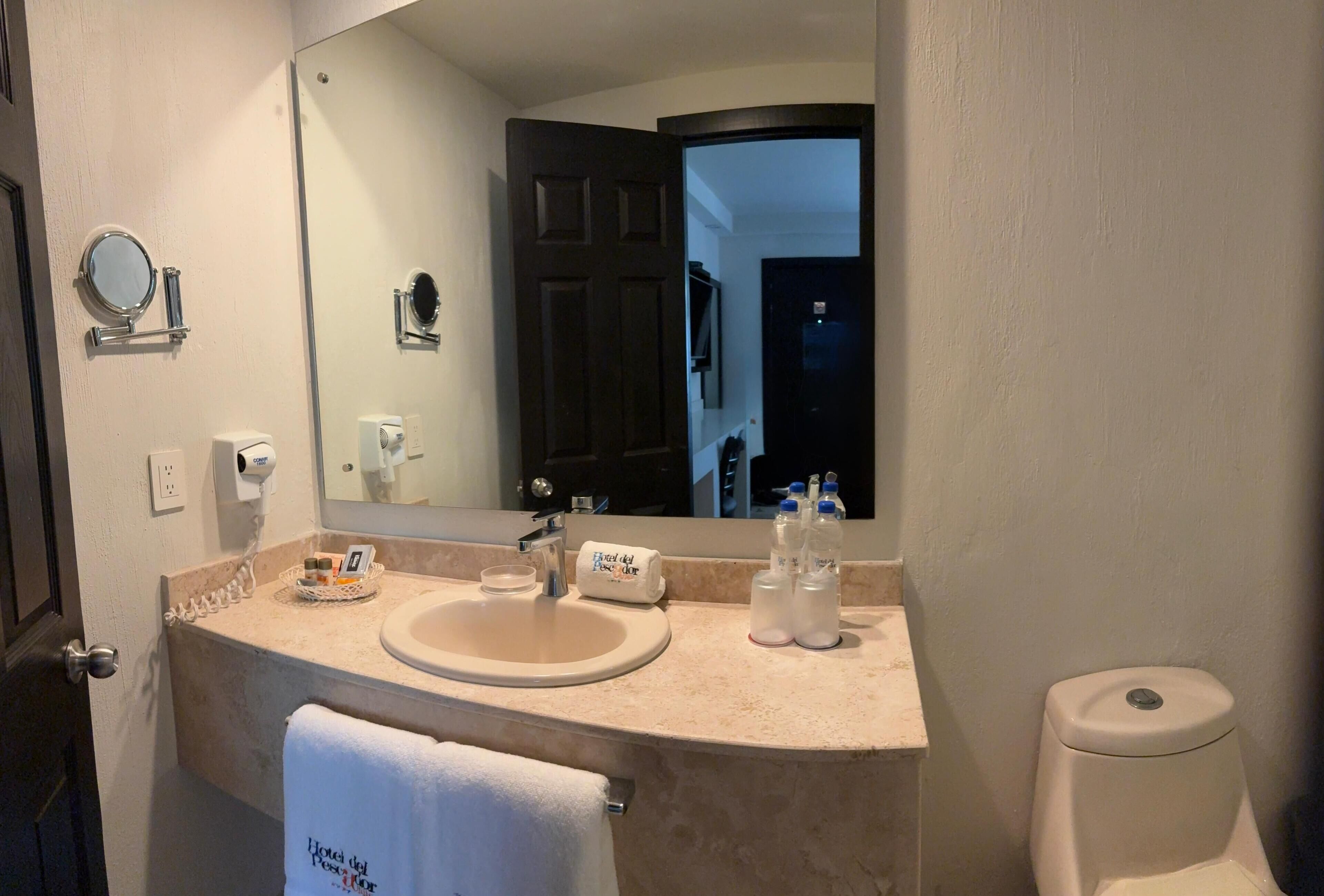 Un baño con lavamanos, espejo, toalla y retrete.