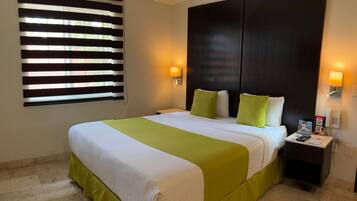 Habitación de hotel con una cama grande, una mesita de noche, un teléfono en la pared y una ventana con persianas.