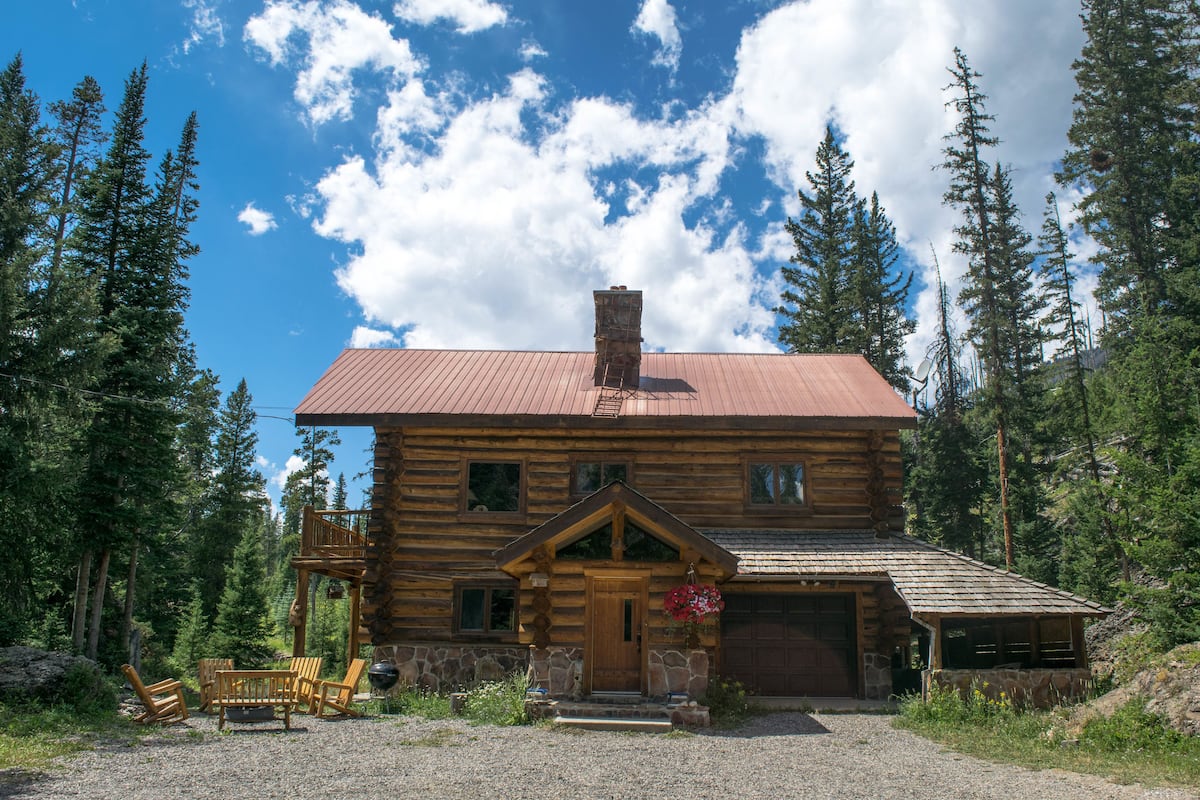 A log cabin with a stone foundation, a wooden porch, and a garage.