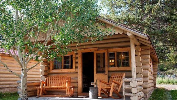 A log cabin with a porch, two wooden benches, and a small table. - Silver Gate Lodging (Silver Gate)