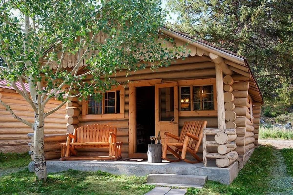 A log cabin with a porch, two wooden benches, and a small table.