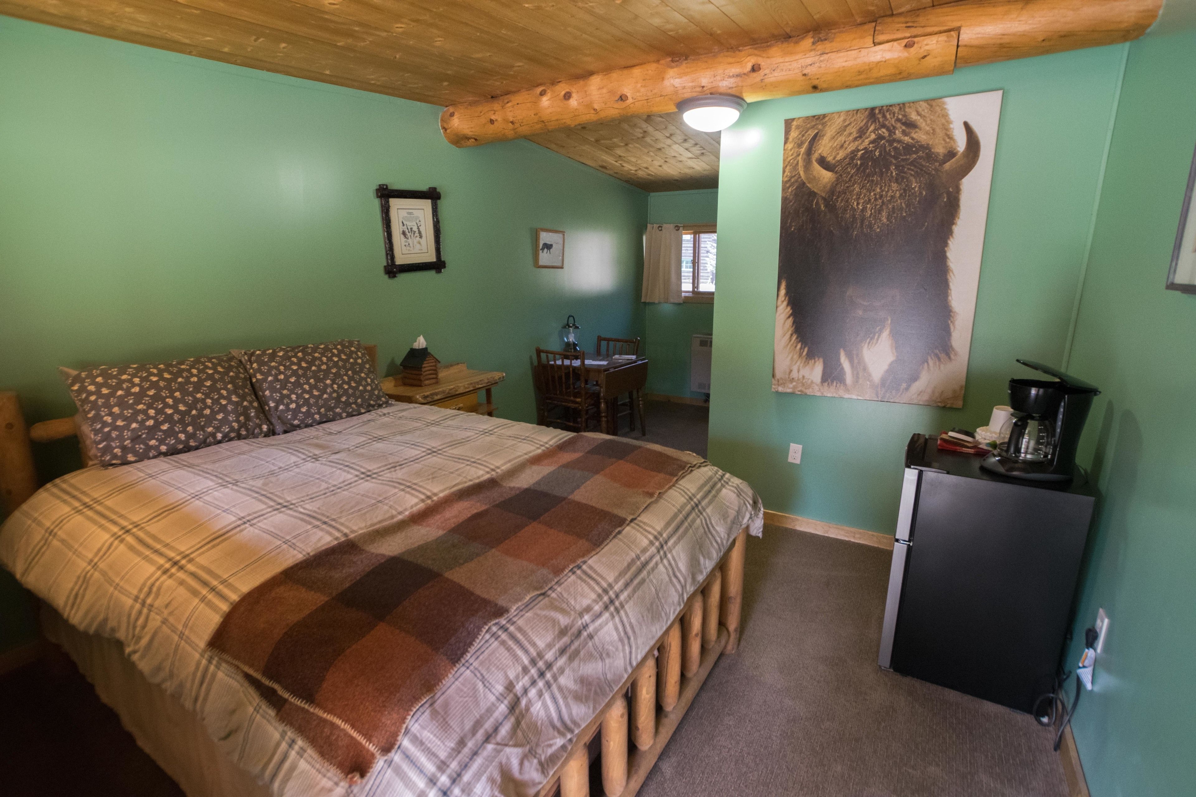 A bedroom with a large bed, a wooden headboard, a desk, and a refrigerator.