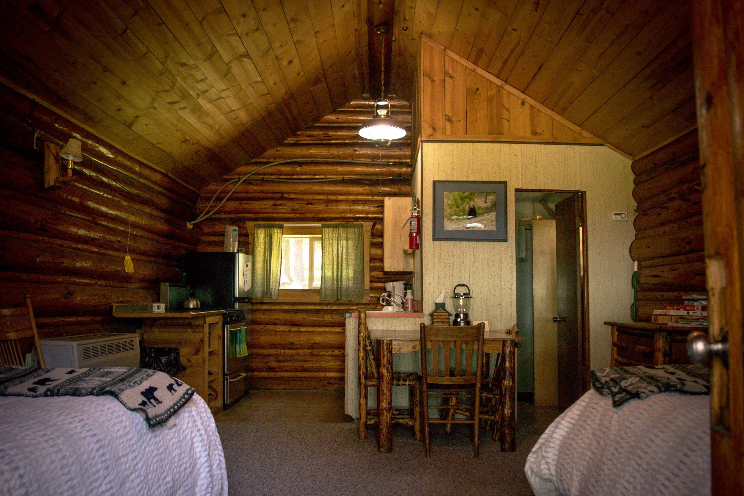 A log cabin interior with two beds, a kitchenette, and a dining area.