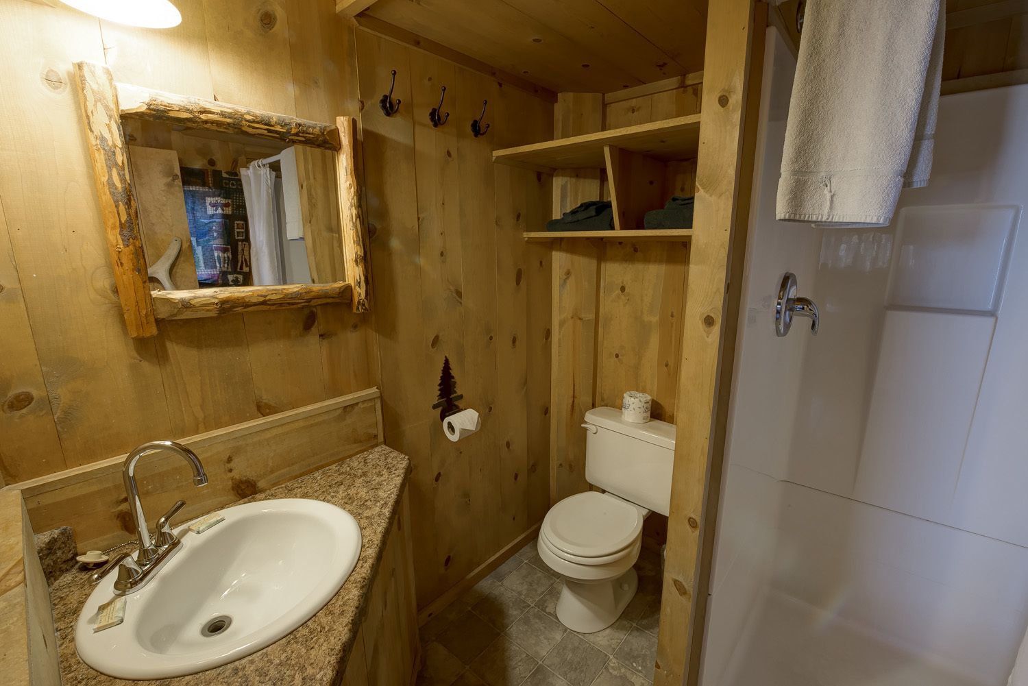 Un baño de madera con lavamanos, inodoro y zona de ducha.