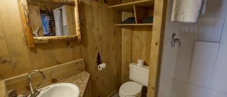 Un baño de madera con lavamanos, inodoro y zona de ducha.