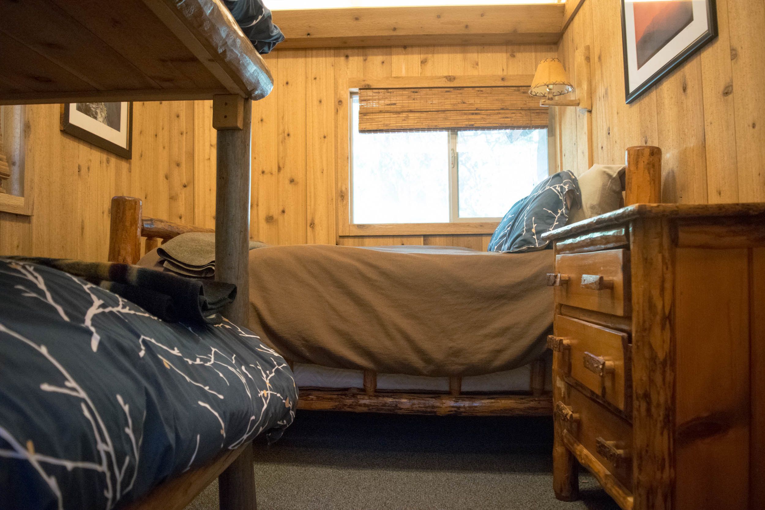 A wooden cabin room with bunk beds, a dresser, and a window.