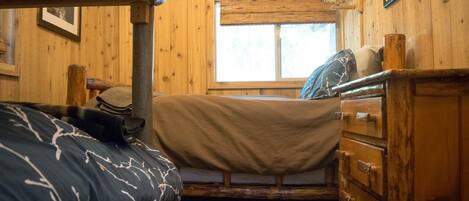 A wooden cabin room with bunk beds, a dresser, and a window.