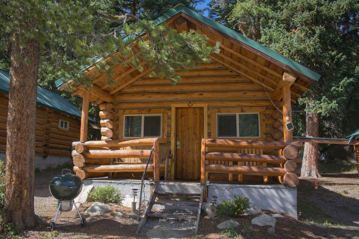 A log cabin with a wooden porch, a front door, and a grill outside.
