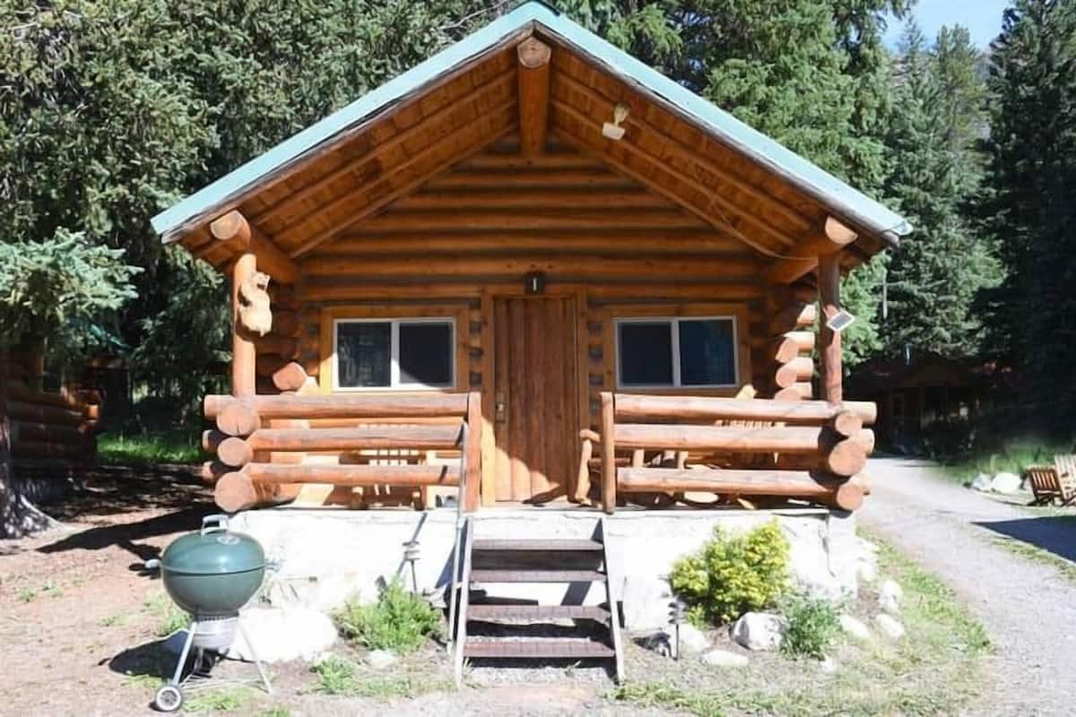 A log cabin with a front porch, a grill, and a staircase leading to the entrance.