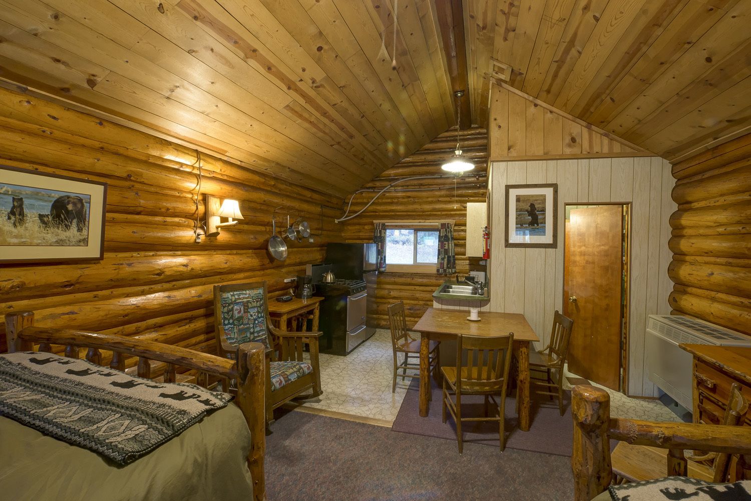 Interior de una cabaña de troncos con comedor, cocina y una zona de estar acogedora con alfombra.