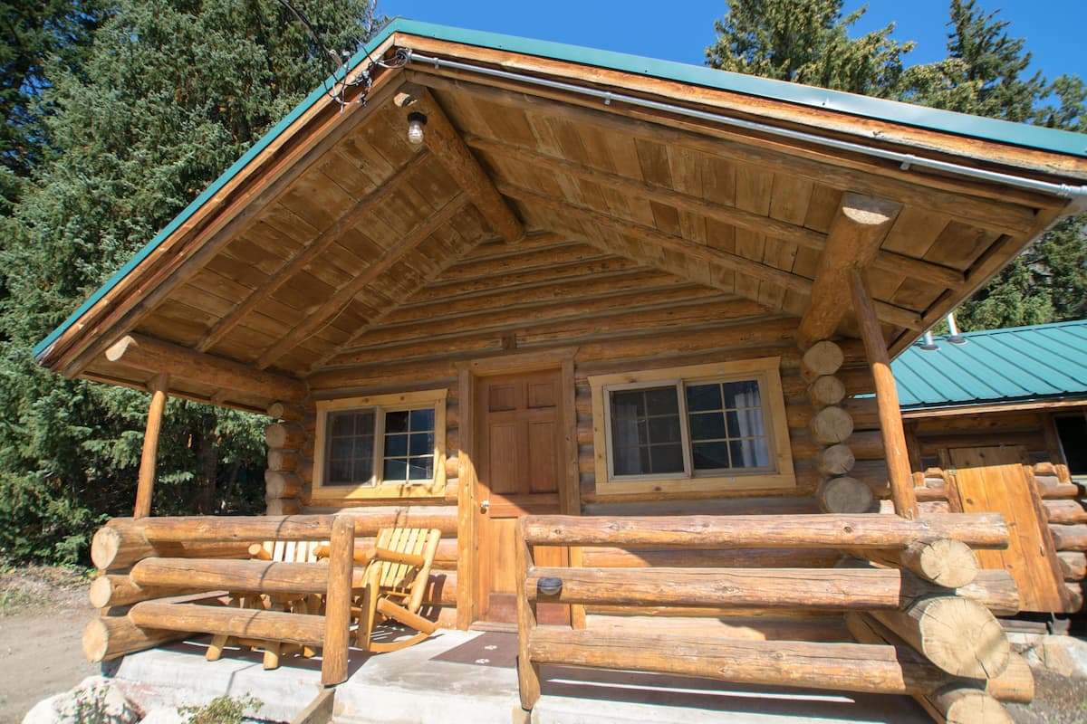 A log cabin with a porch, wooden exterior, and a green roof.
