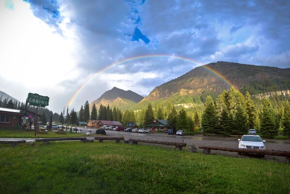 A mountain landscape with a rainbow, a parking area, and a cabin named "Pine Ridge Cabins". - Silver Gate Lodging (Silver Gate)