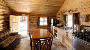 A wooden cabin interior with a dining table, chairs, a kitchen with a stove, refrigerator, and a sink. - Silver Gate Lodging (Silver Gate)