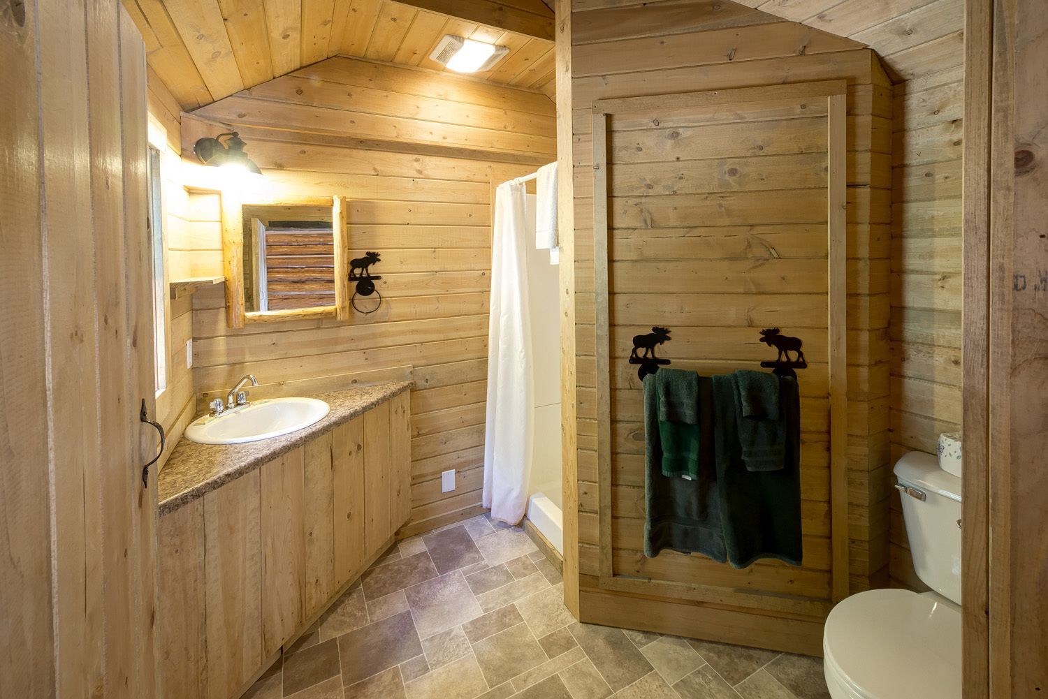 A wooden cabin bathroom with a sink, mirror, and toilet.