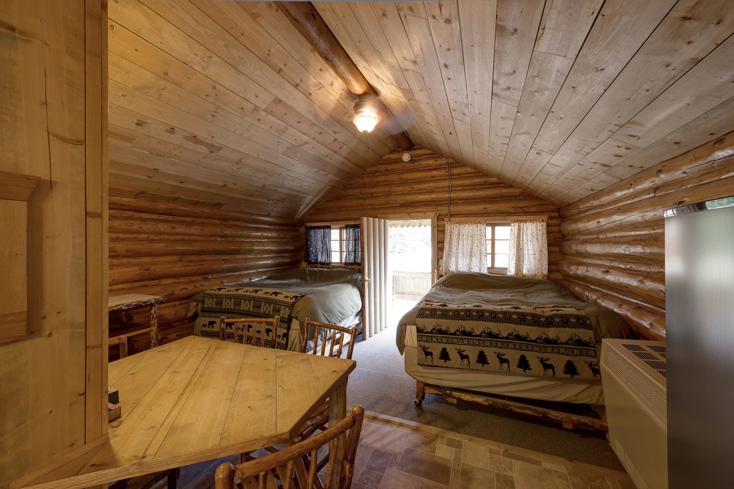 Ein Zimmer in einer Blockhütte mit einem Bett, einem Tisch und einem Stuhl.