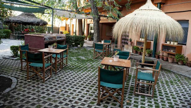 An outdoor patio with thatched umbrellas, wooden tables, and green chairs. - Hostel Layos, Toledo (Layos)
