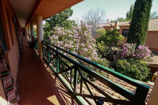 A balcony with a tiled floor, a green railing, and a view of pink flowering trees and a tall evergreen tree.
