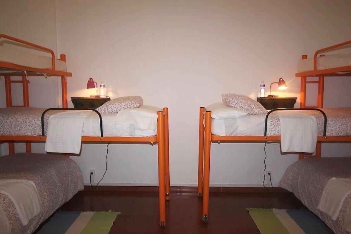 Habitación tipo dormitorio con dos literas, cada una con una almohada y una mesita de noche con lámpara.