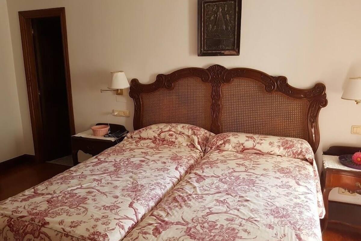 A hotel room with a large bed, two bedside tables, a nightstand, a door, and a framed picture on the wall.