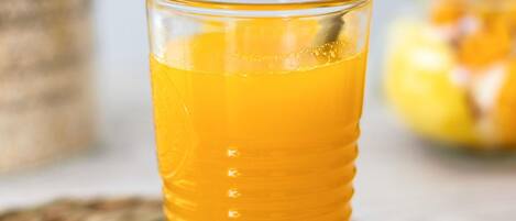 A glass of orange juice with a straw, placed on a woven coaster.