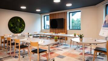 A conference room with a large round table, multiple chairs, a flat-screen TV, and a large window.