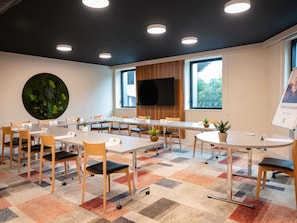 Een vergaderruimte met een grote ronde tafel, meerdere stoelen, een flatscreen televisie en een groot raam.