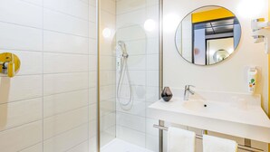 Une salle de bain moderne avec une douche à parois de verre, un lavabo blanc et un miroir rond.