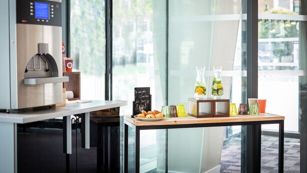 Une machine à café moderne, une table en bois avec des pâtisseries et un panneau noir dans une pièce lumineuse dotée de grandes fenêtres.