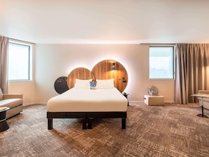 A hotel room with a large bed, a bedside table, a chair, a desk, and a view of the city through the window. - ibis Styles Paris Meteor Avenue d'Italie (Paris)