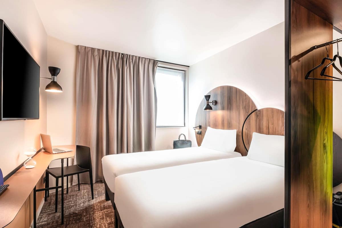 A hotel room with a bed, a desk, a chair, a TV, and a window with curtains.