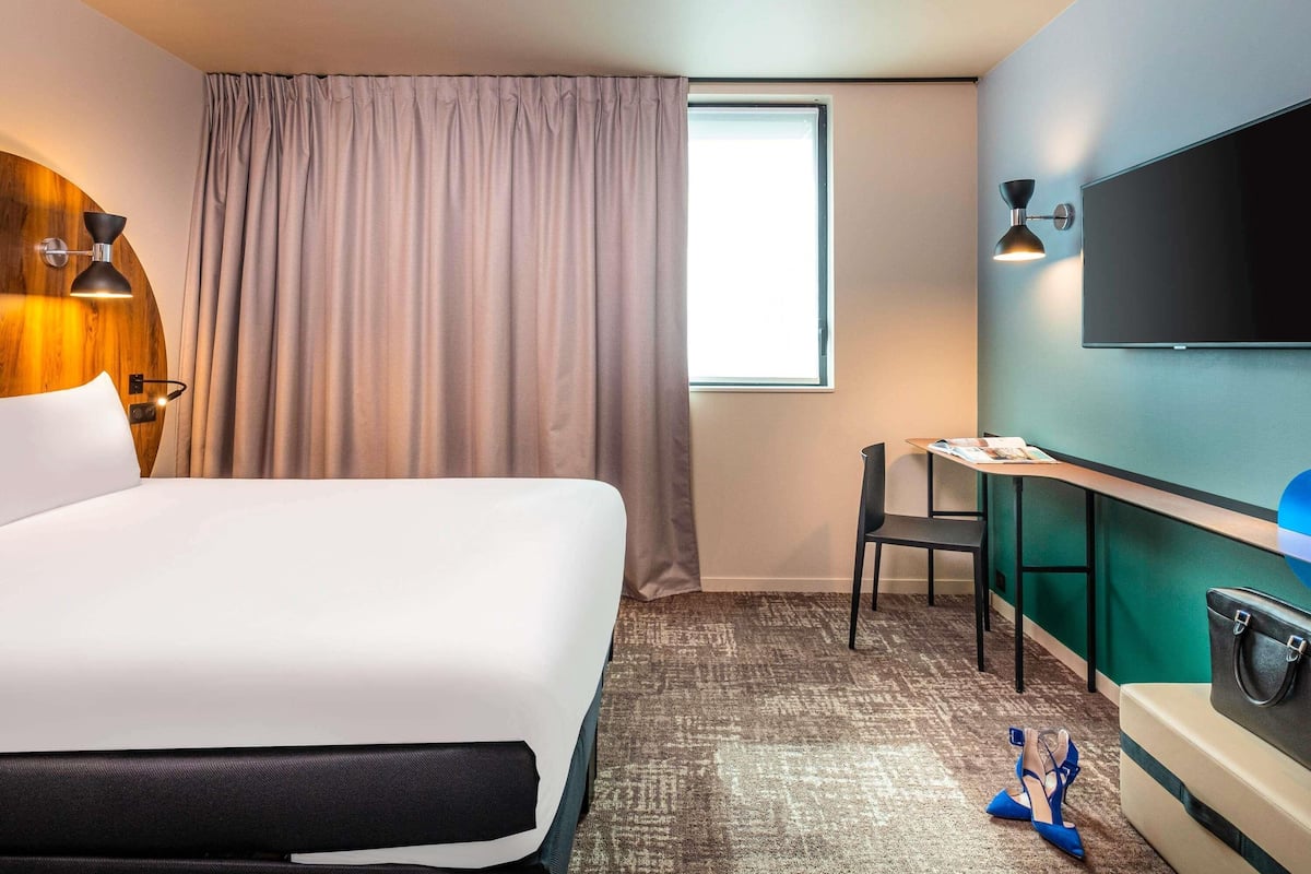 Hotellihuone, jossa on sänky, työpöytä, tuoli, televisio ja ikkuna, jossa on verhot.
