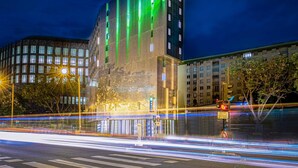 Un bâtiment moderne à la façade distinctive, illuminée de vert, avec une entrée bien visible et une vue dégagée sur l’environnement urbain qui l’entoure.