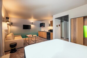 A hotel room with a bed, a sofa, a small table, a kitchen area, and a TV. - ibis Styles Paris Meteor Avenue d'Italie (Paris)