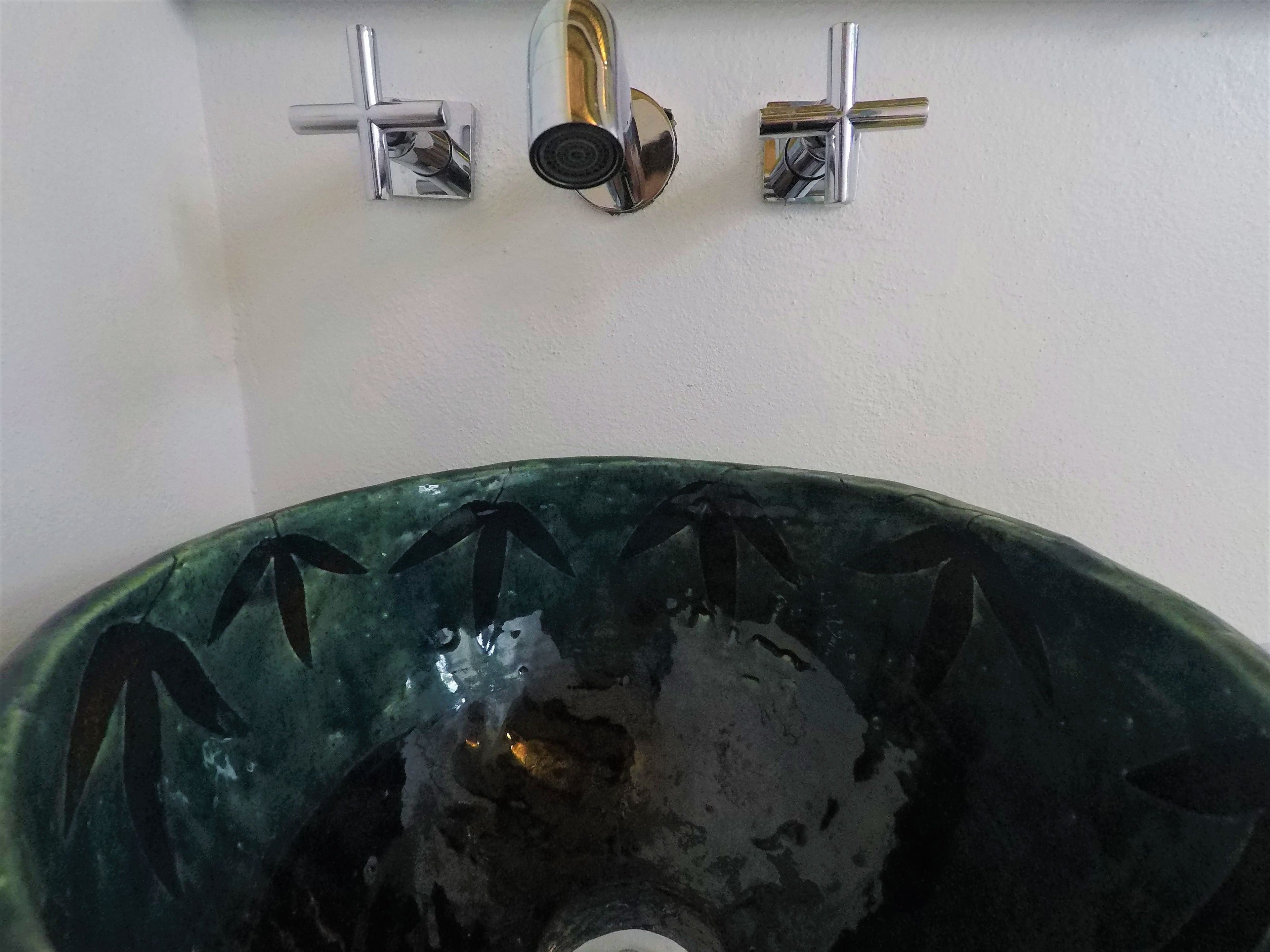 Un lavabo de cerámica verde con un grifo en forma de cruz y un caño de un solo mando.