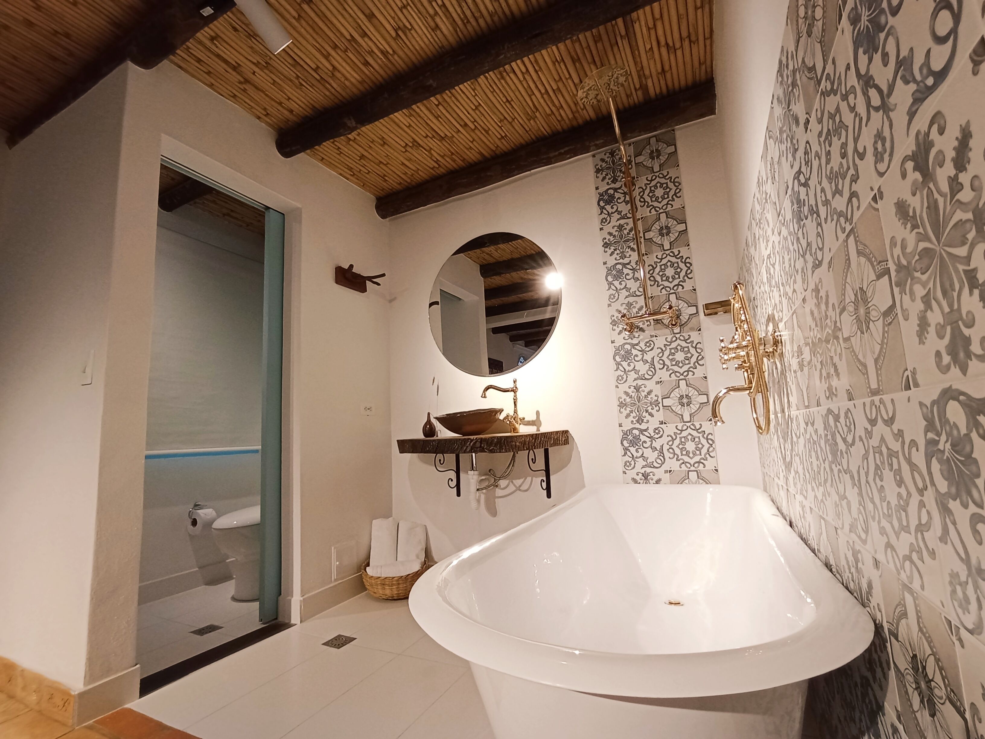 A bathroom with a freestanding bathtub, a round mirror, a sink with a decorative basin, and patterned wall tiles.