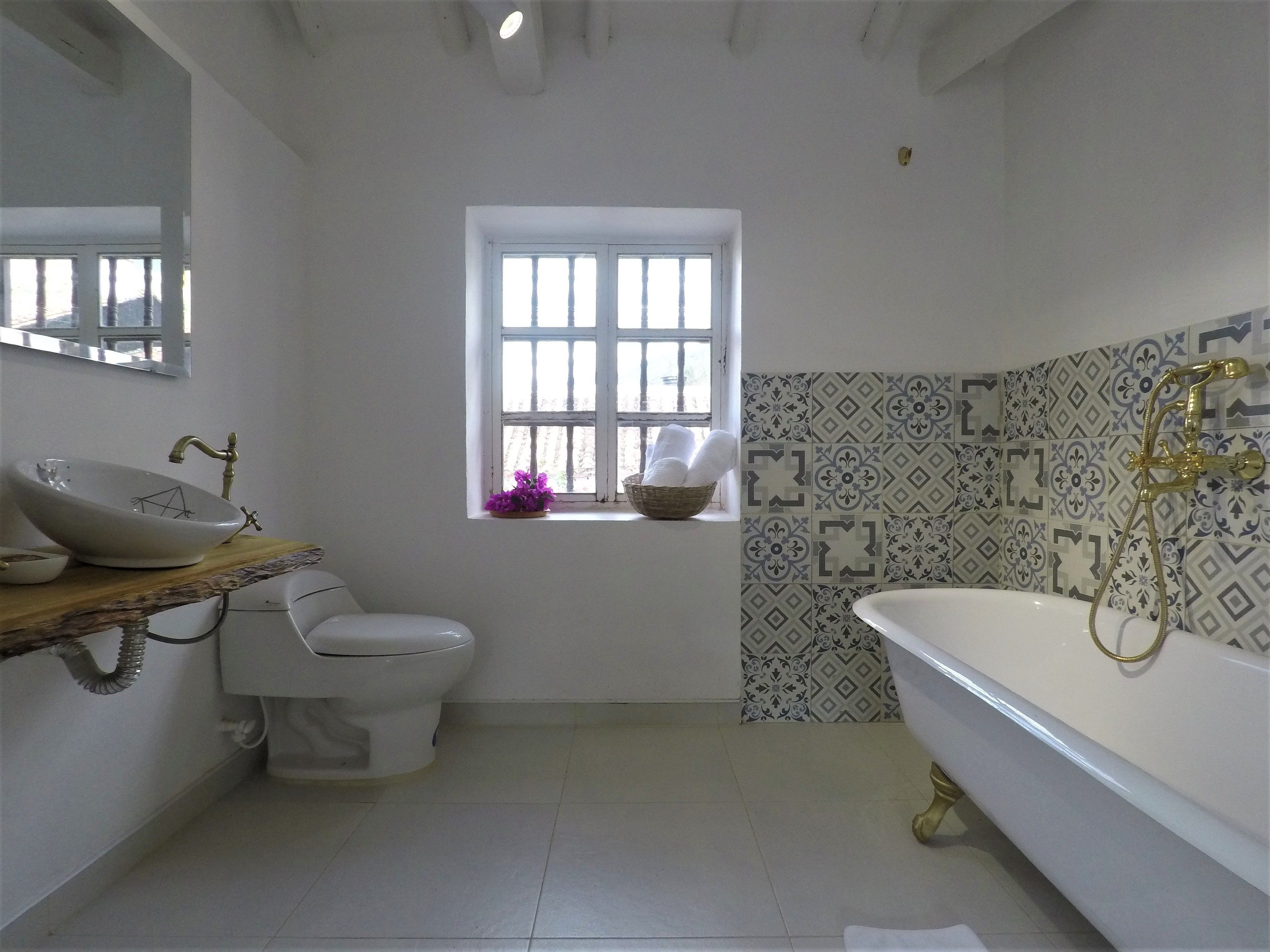 A bathroom with a white sink, a toilet, a bathtub, and a window with a basket of towels.