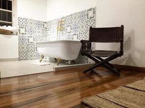 Un baño con una bañera independiente, una silla de madera y baldosas decorativas en las paredes.